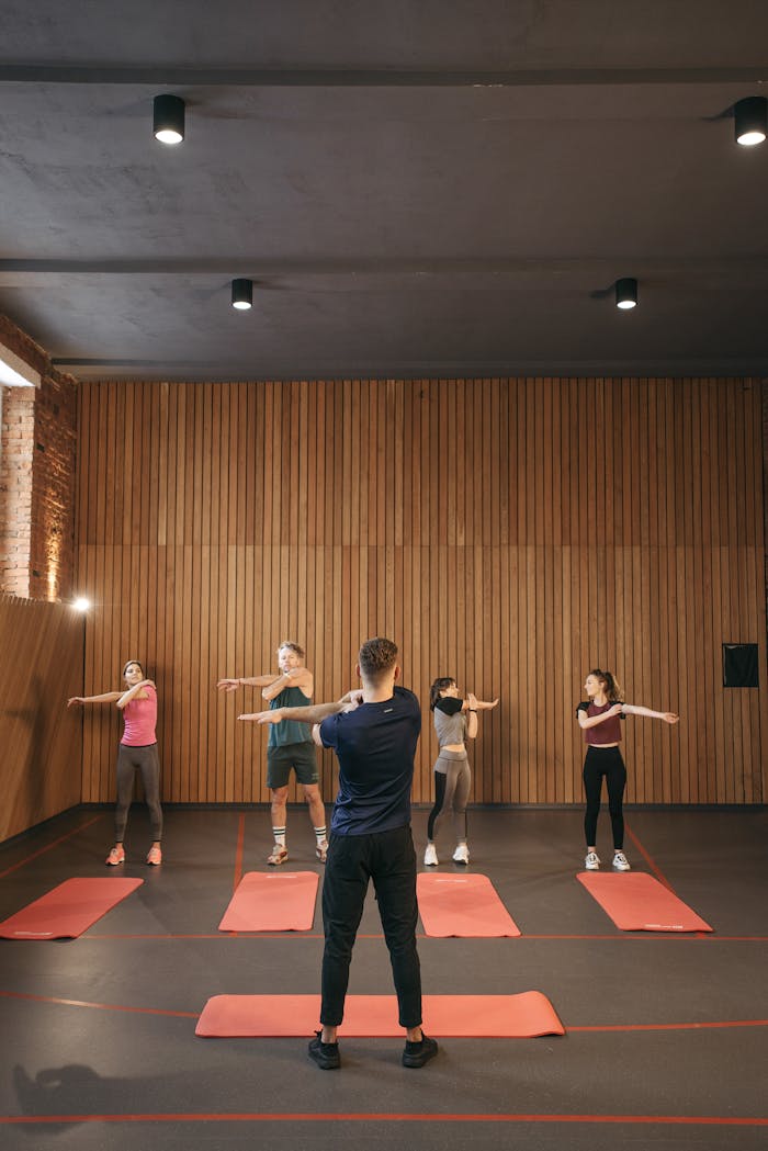 services-03 A diverse group of adults stretching together in an indoor fitness class, led by an instructor.