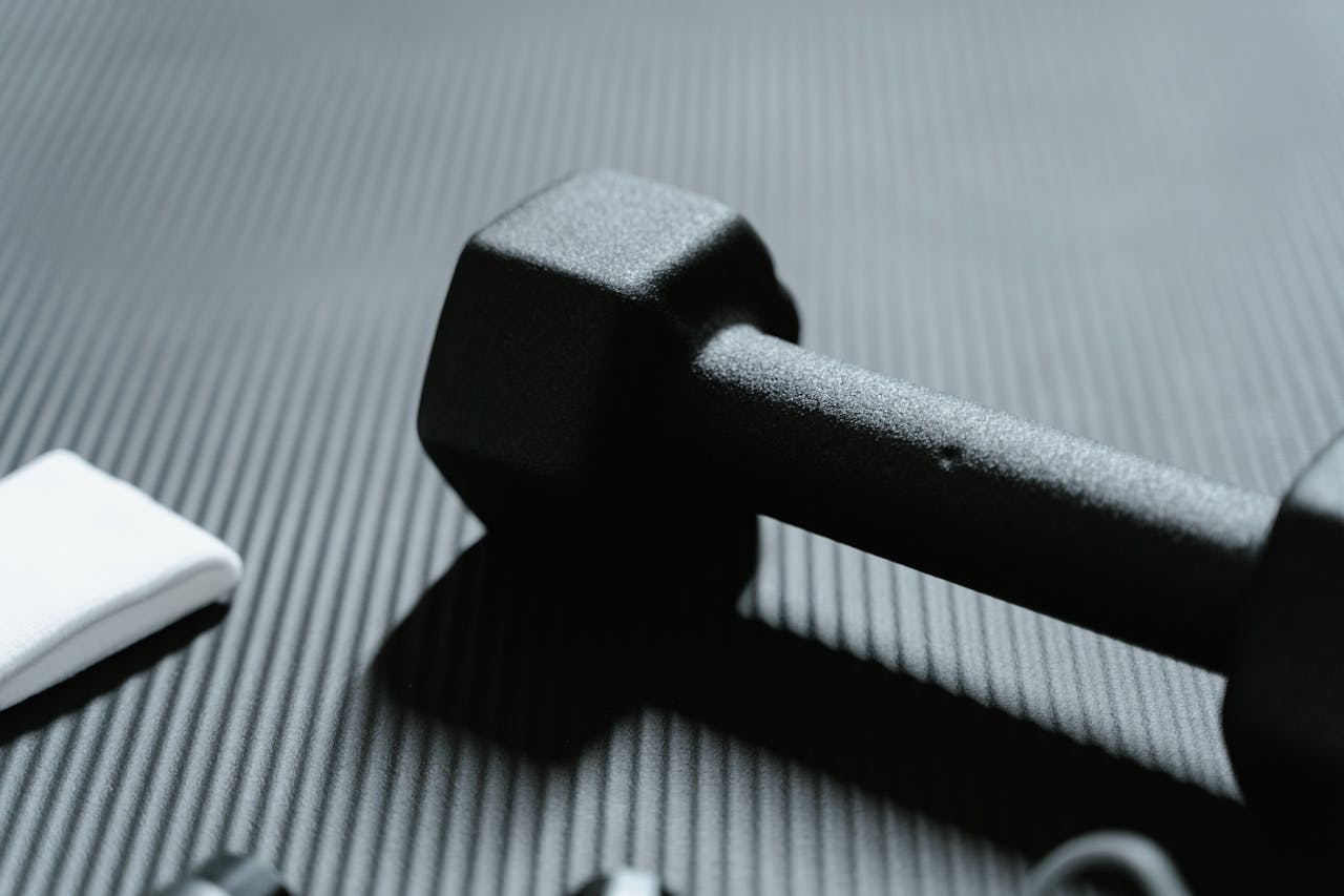 gallery-1 Detailed view of a black dumbbell on textured mat for fitness workout